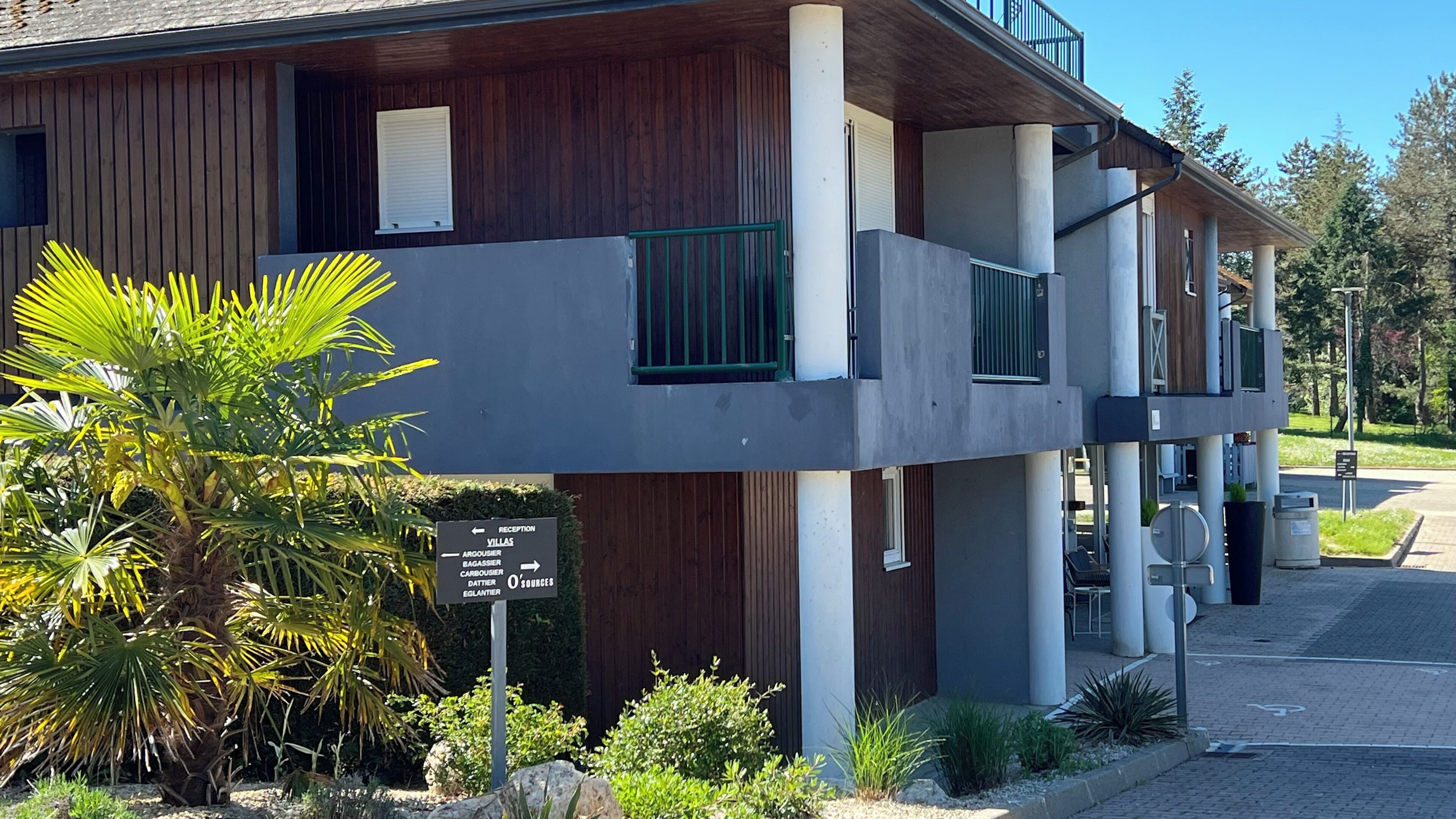 A two-story building with a reception desk, a sign indicating directions to villas, and a balcony with a metal railing.
