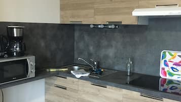 A modern kitchen with wooden cabinets, a black countertop, a microwave, a coffee maker, and a colorful tray.