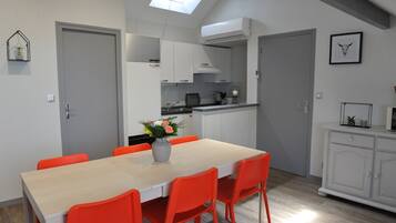 Une cuisine moderne avec des meubles blancs, une table à manger entourée de chaises orange et une lucarne au-dessus.