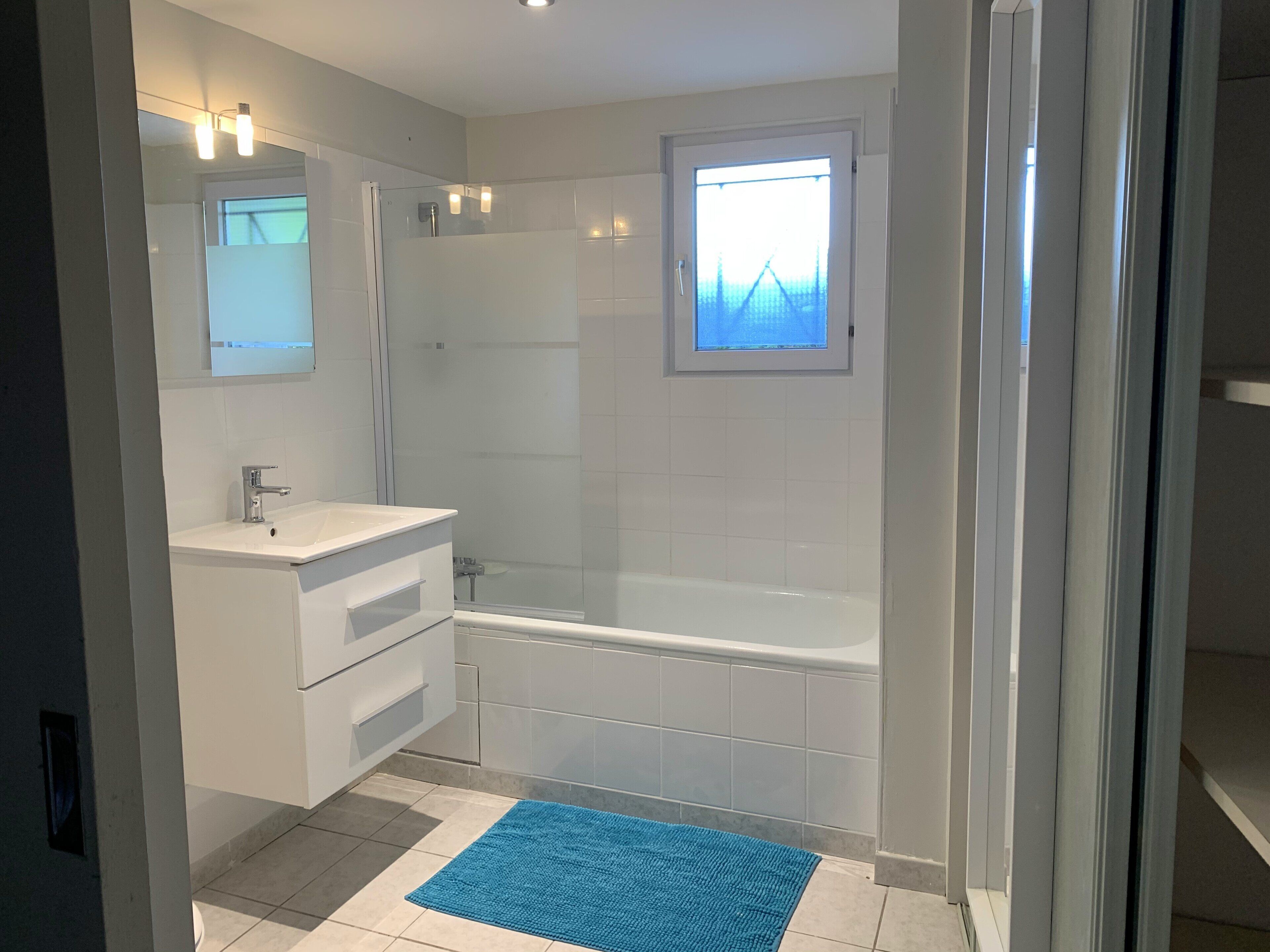 Un baño moderno con tocador blanco, cabina de ducha de vidrio y alfombra de baño azul.