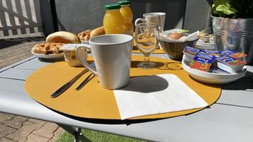 A breakfast table with a waffle, a mug, a glass, a bottle of juice, a bowl of yogurt, and a potted plant.