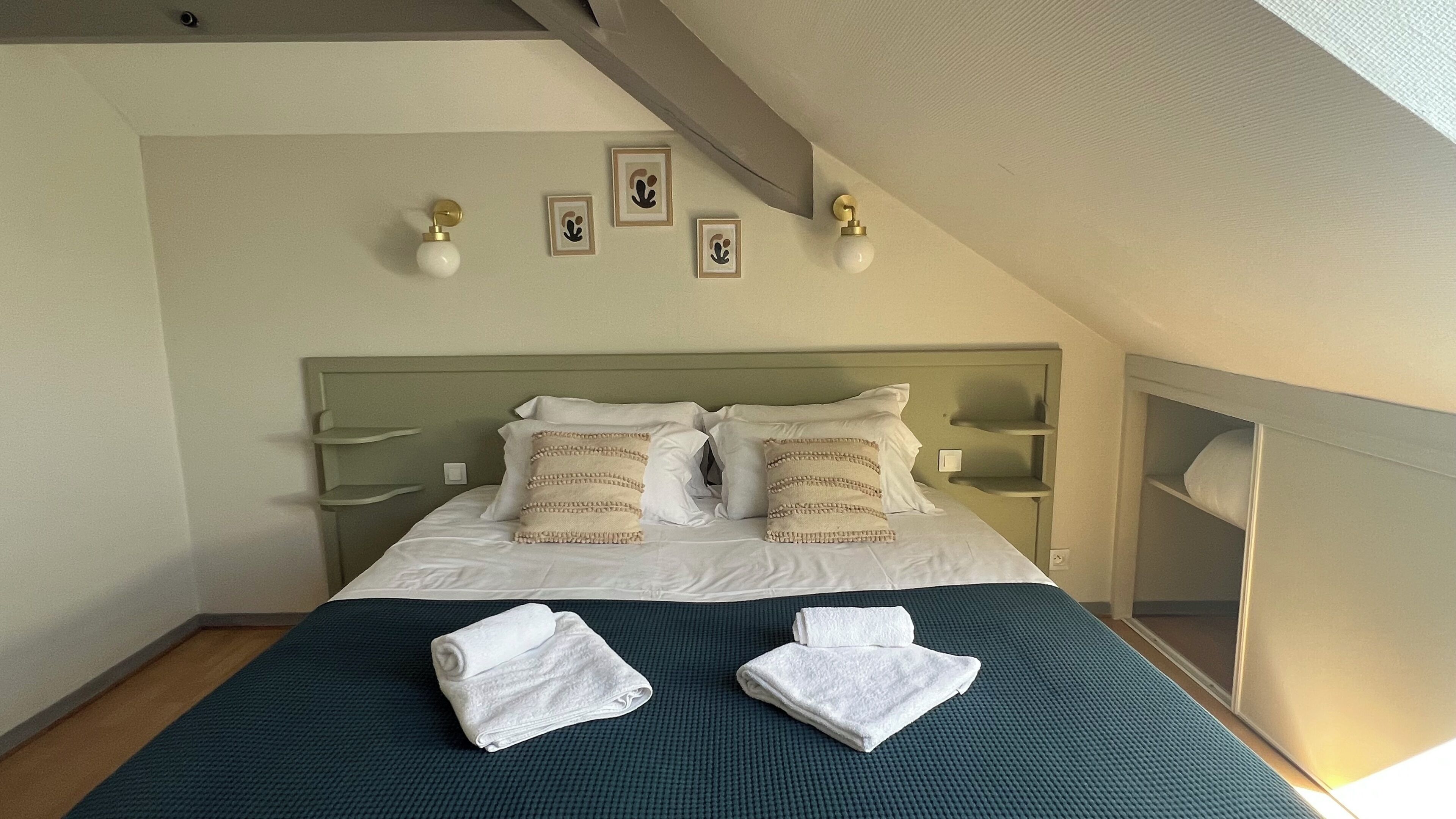 A neatly made bed with pillows, a headboard, bedside tables, and wall-mounted lights.