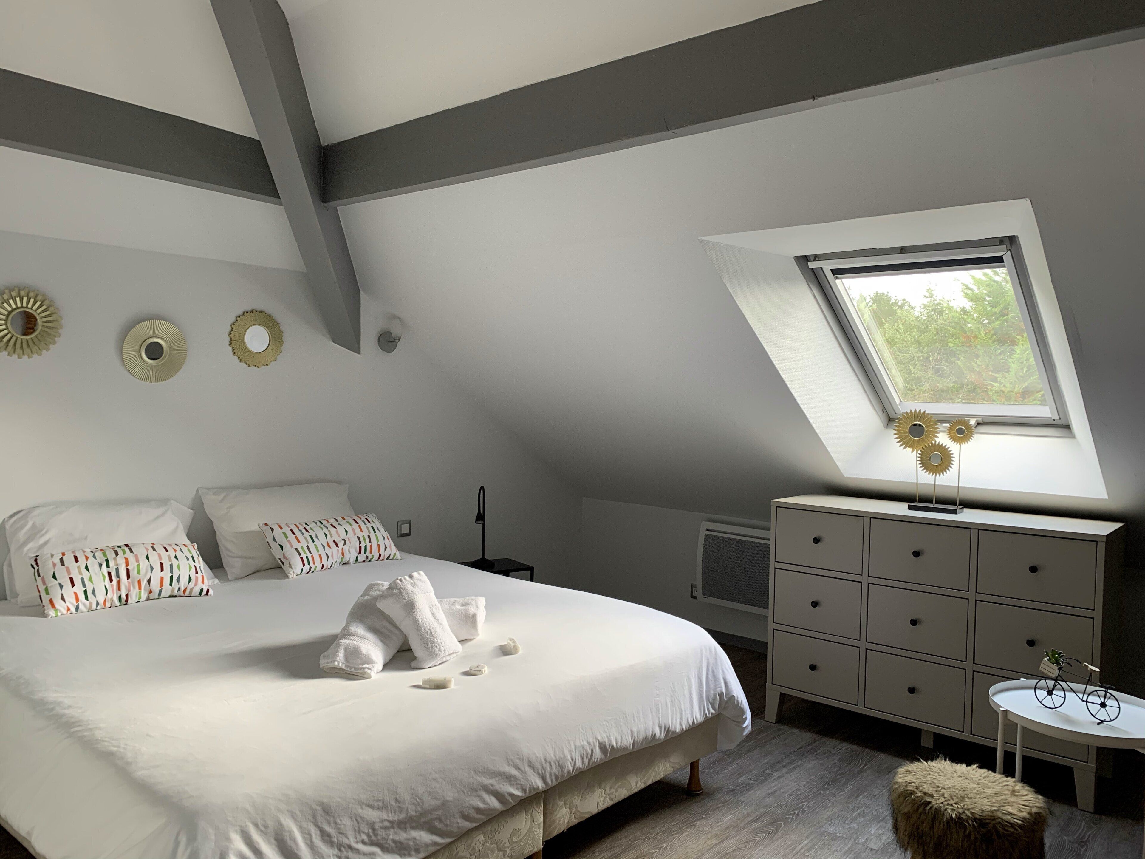 A bedroom with a bed, a dresser, a small table, a window, and decorative wall mirrors.