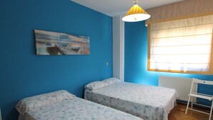 Ein Zimmer mit zwei Einzelbetten, einem Bild an der Wand, einem Fenster mit Vorhängen und einem weißen Stuhl.