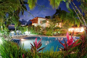 A pool area with lounge chairs, surrounded by tropical plants and a house in the background. - Villas Nicolás - Adults Only (Quepos)