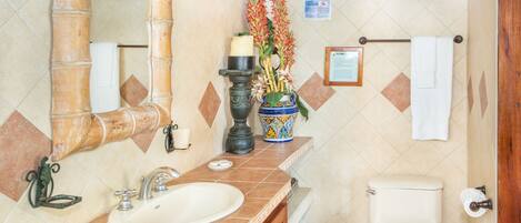 A bathroom with a sink, mirror, toilet, and a decorative vase with flowers.