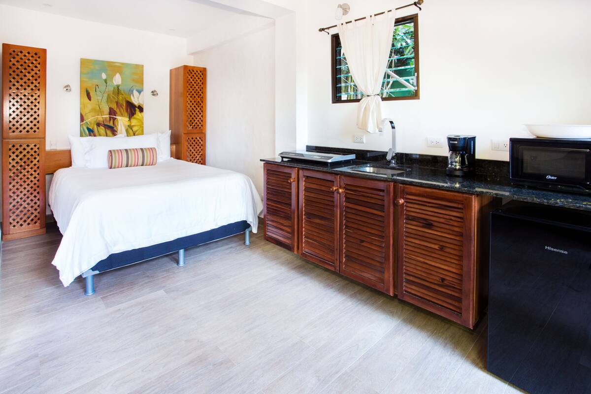 A hotel room with a bed, wooden cabinets, a microwave, and a sink.