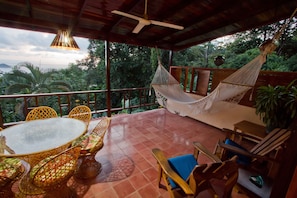 A covered outdoor seating area with a table and chairs, a hammock, and a view of the surrounding greenery. - Villas Nicolás - Adults Only (Quepos)