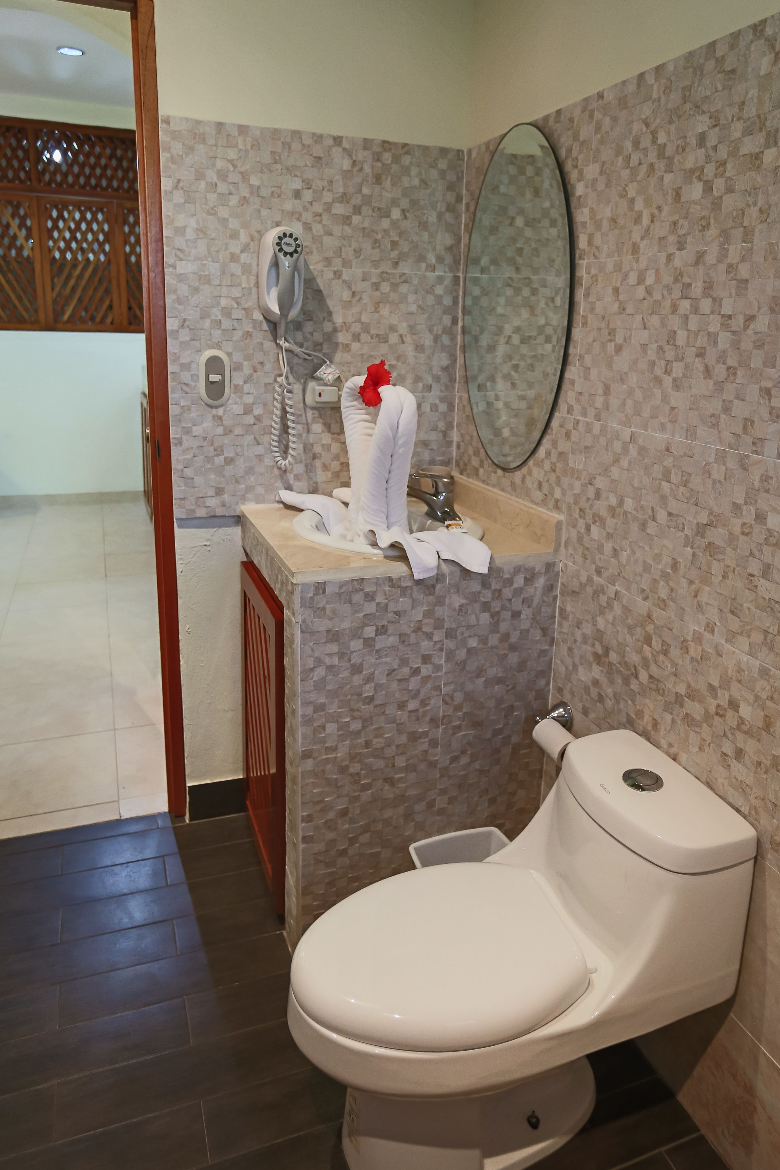 Un baño con inodoro, lavamanos con espejo y un secador de pelo en la pared.