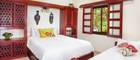Un dormitorio con una cama grande, una cama más pequeña, muebles de madera y una ventana con vistas a la vegetación.