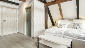Une chambre avec un plafond en bois, un lit avec une literie blanche, une table de chevet et une porte.