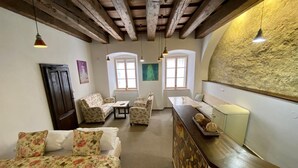 Une pièce confortable avec un lit, un canapé, un fauteuil, une petite table et un comptoir sur lequel se trouve une lampe. Il y a des fenêtres et une porte.