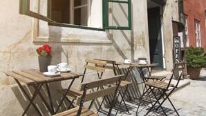 Un café en plein air avec des tables et des chaises en bois, une plante en pot et un panneau indiquant que l’établissement est ouvert.