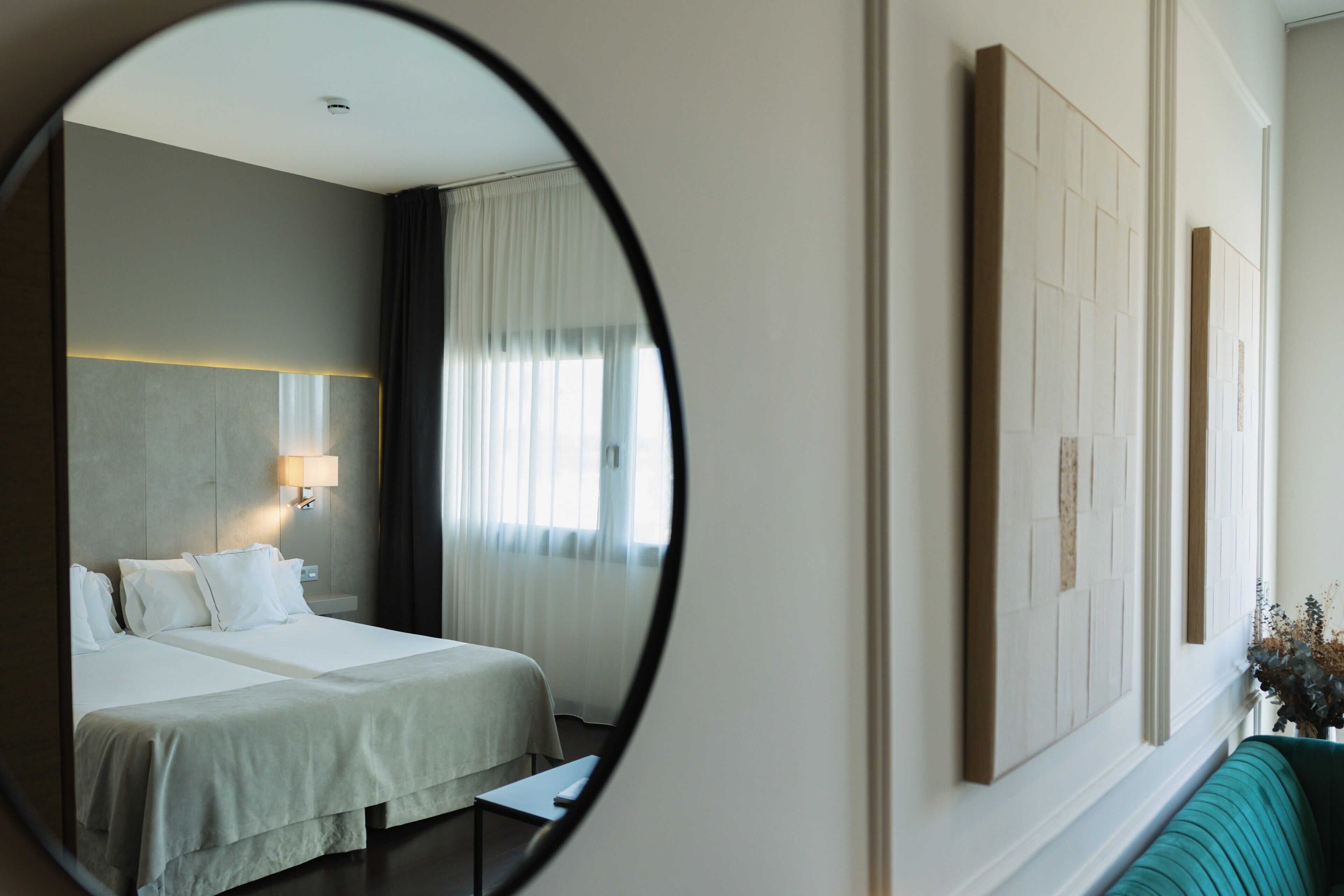 Une chambre d’hôtel avec un lit, une table de chevet, une lampe et un miroir qui reflète la pièce.