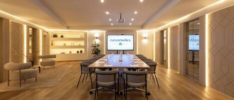 Une salle de conférence équipée d’une longue table, de chaises, d’un écran de projection et d’une enseigne « GreenSuites ».