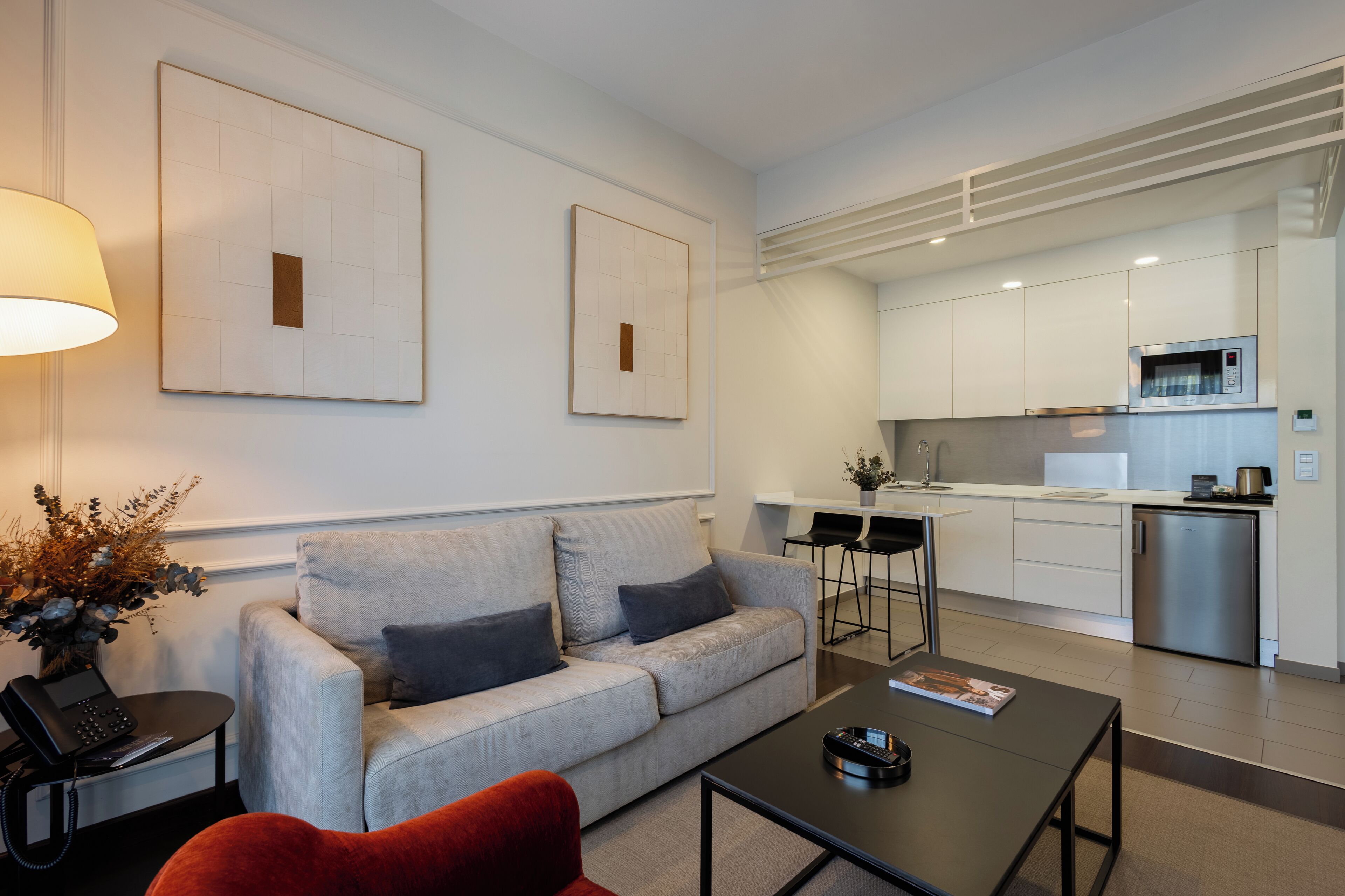 A modern living room with a grey sofa, a red armchair, a coffee table, and a dining area with a kitchen in the background.