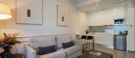 A modern living room with a grey sofa, a red armchair, a coffee table, and a dining area with a kitchen in the background.