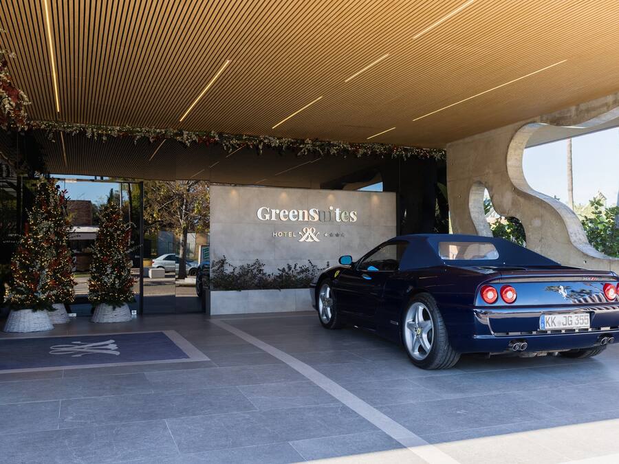 Ein Hotel Eingang mit einem dunkelblauen Cabrio, einem Schild für 'GreenSuites Hotel' und einer Weihnachtsbäume-Ausstellung.