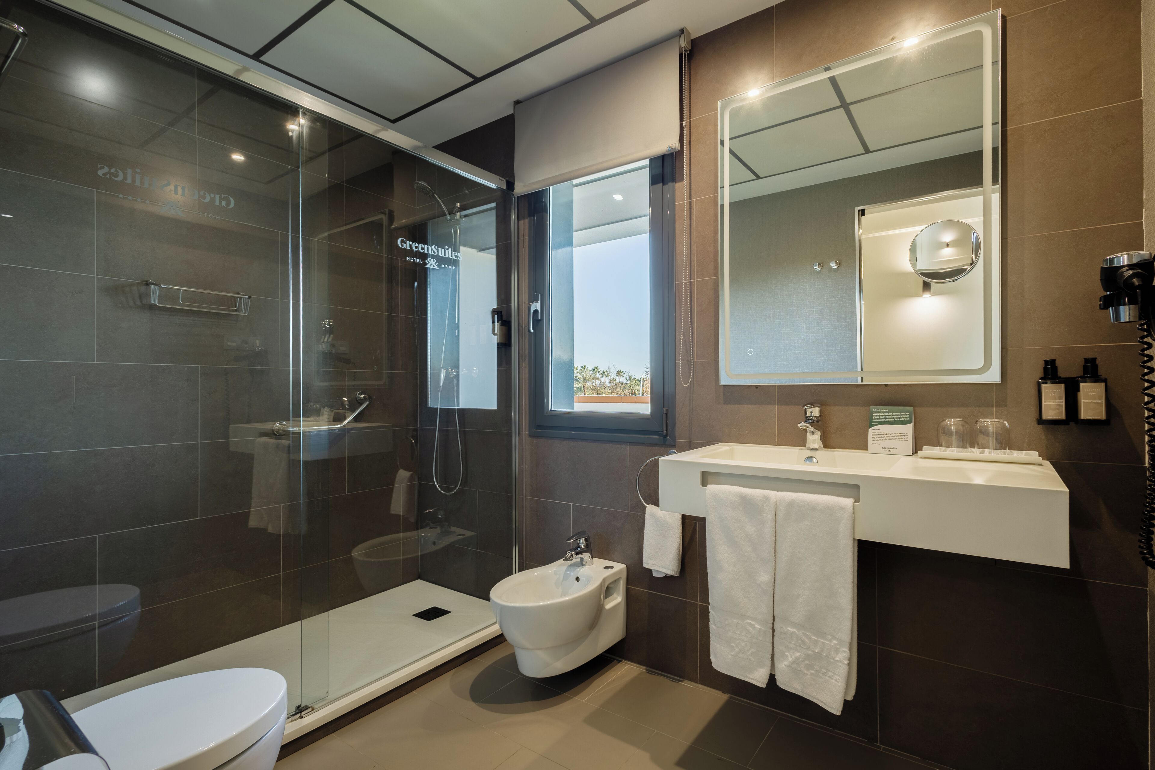 A modern bathroom with a glass-enclosed shower, a bidet, a toilet, and a vanity with a mirror.