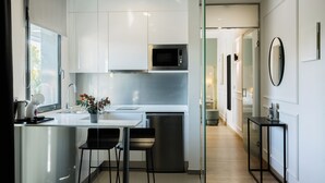 Una cocina moderna con armarios blancos, un refrigerador de acero inoxidable, microondas integrado y una pequeña isla con taburetes de bar.