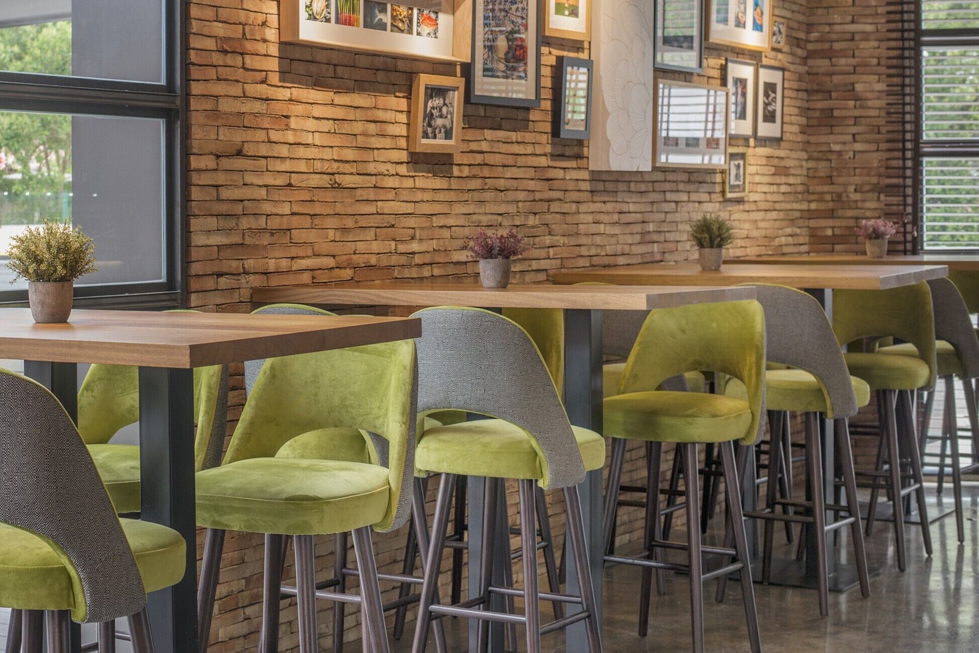 A modern bar area with green upholstered bar stools, a wooden bar counter, and a brick wall adorned with framed artwork.