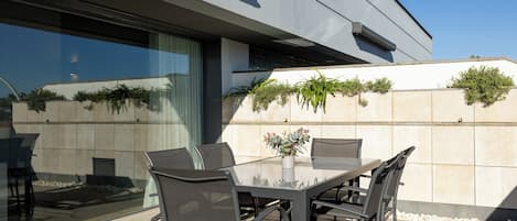 An outdoor patio with a glass table and chairs, a potted plant, and a view of the building's exterior.