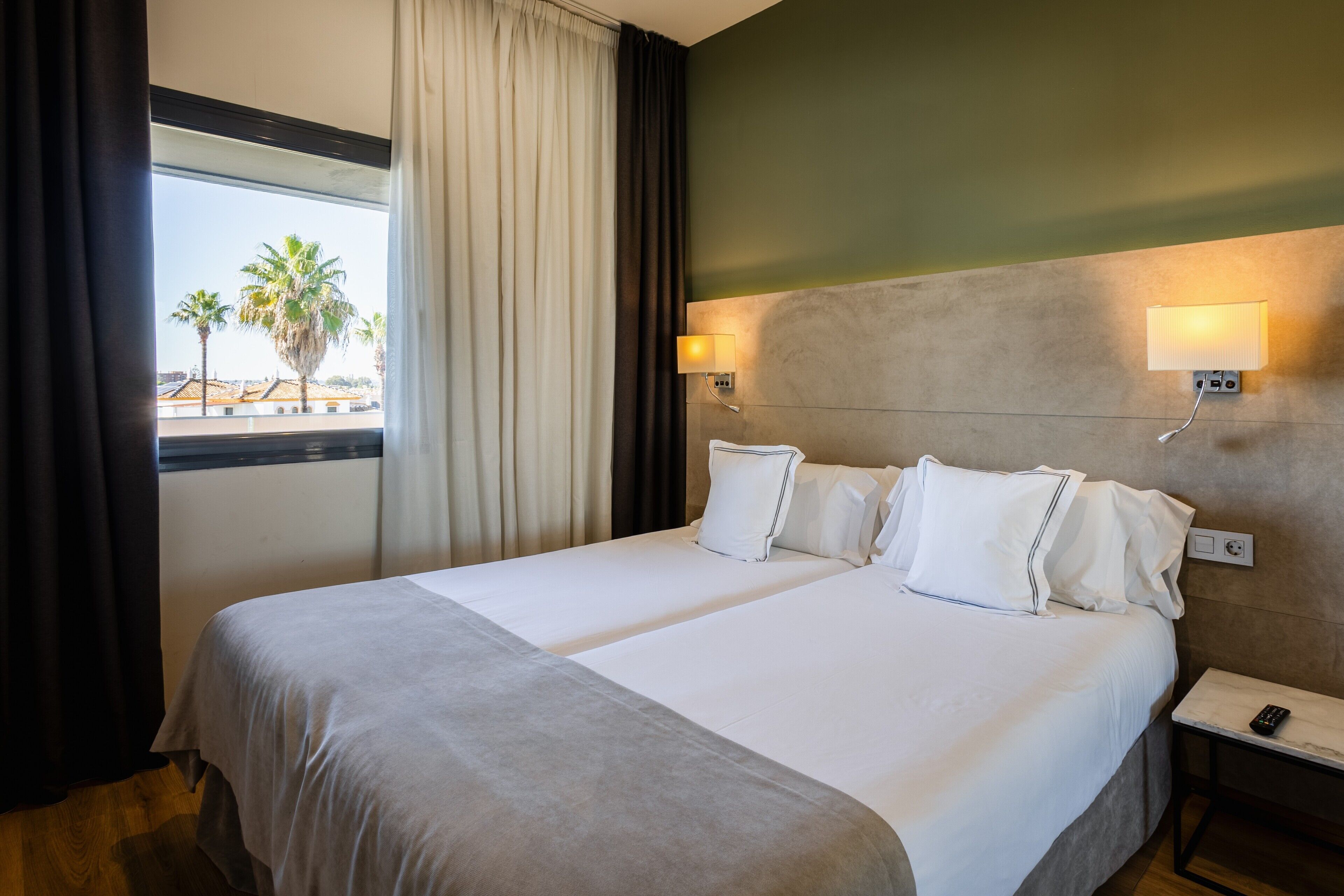 A hotel room with two beds, a view of palm trees, and a window with curtains.