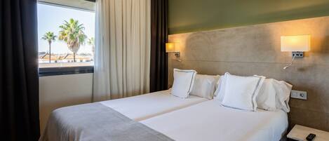 Habitación de hotel con dos camas, vista a palmeras y ventana con cortinas.
