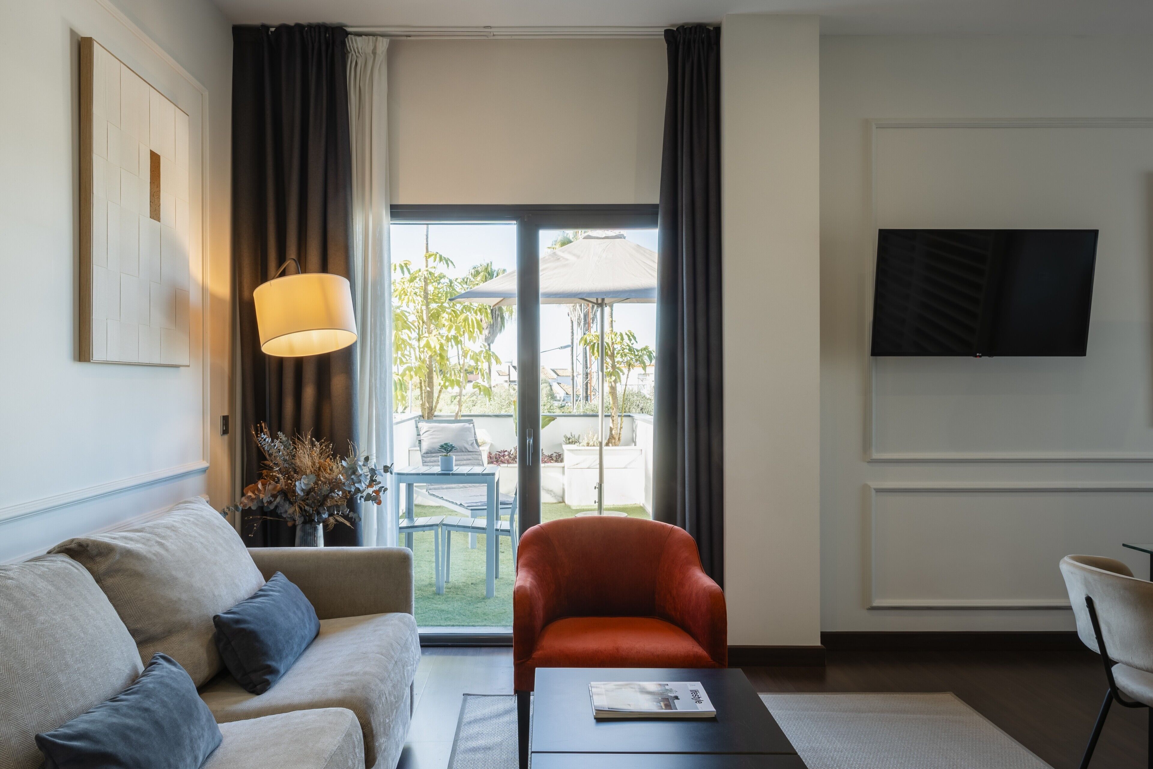 Ein modernes Hotelzimmer mit Sofa, Ohrensessel, Flachbildfernseher und Blick ins Freie.
