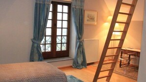 Une chambre à coucher avec un lit, une fenêtre avec des rideaux, un radiateur et une échelle en bois.