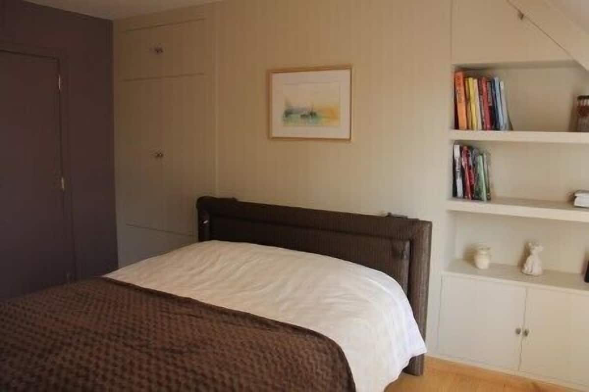 A bedroom with a bed, a bookshelf with books, and a framed picture on the wall.