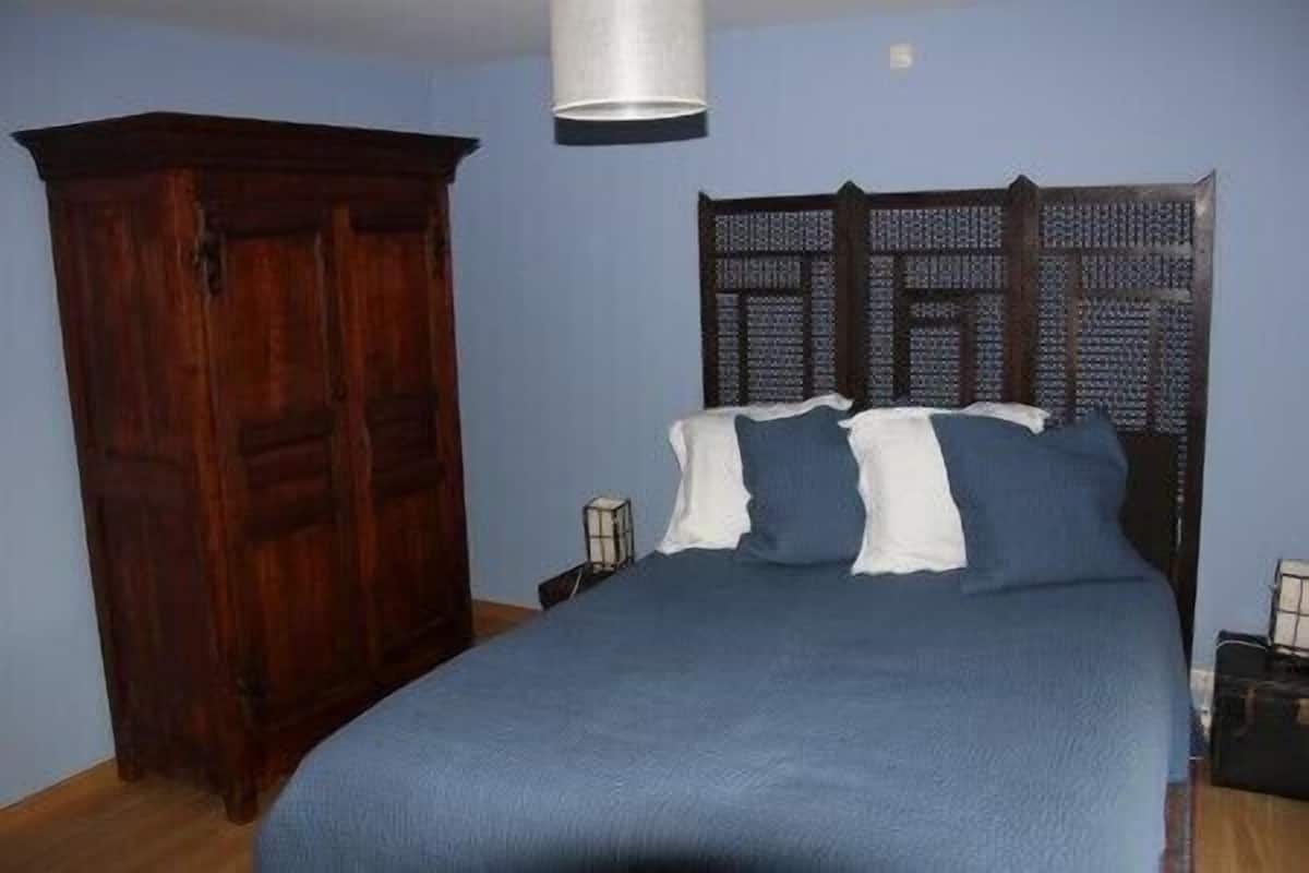 A bedroom with a wooden wardrobe, a bed with blue bedding, and a patterned headboard.