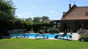 Une maison avec un toit en tuiles, une piscine et un espace salon extérieur.