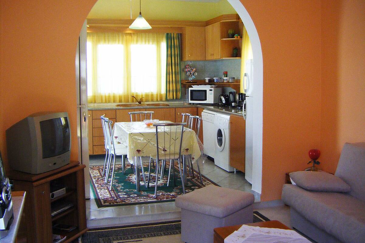 A living room with a television, a sofa, a dining table with chairs, and a kitchen area with appliances.