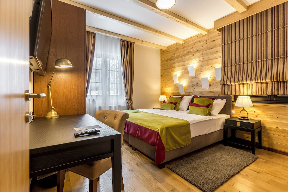 Ein Hotelzimmer mit Bett, Nachttisch, Lampe, Schreibtisch, Stuhl und einer Holzwand mit Wandleuchten.