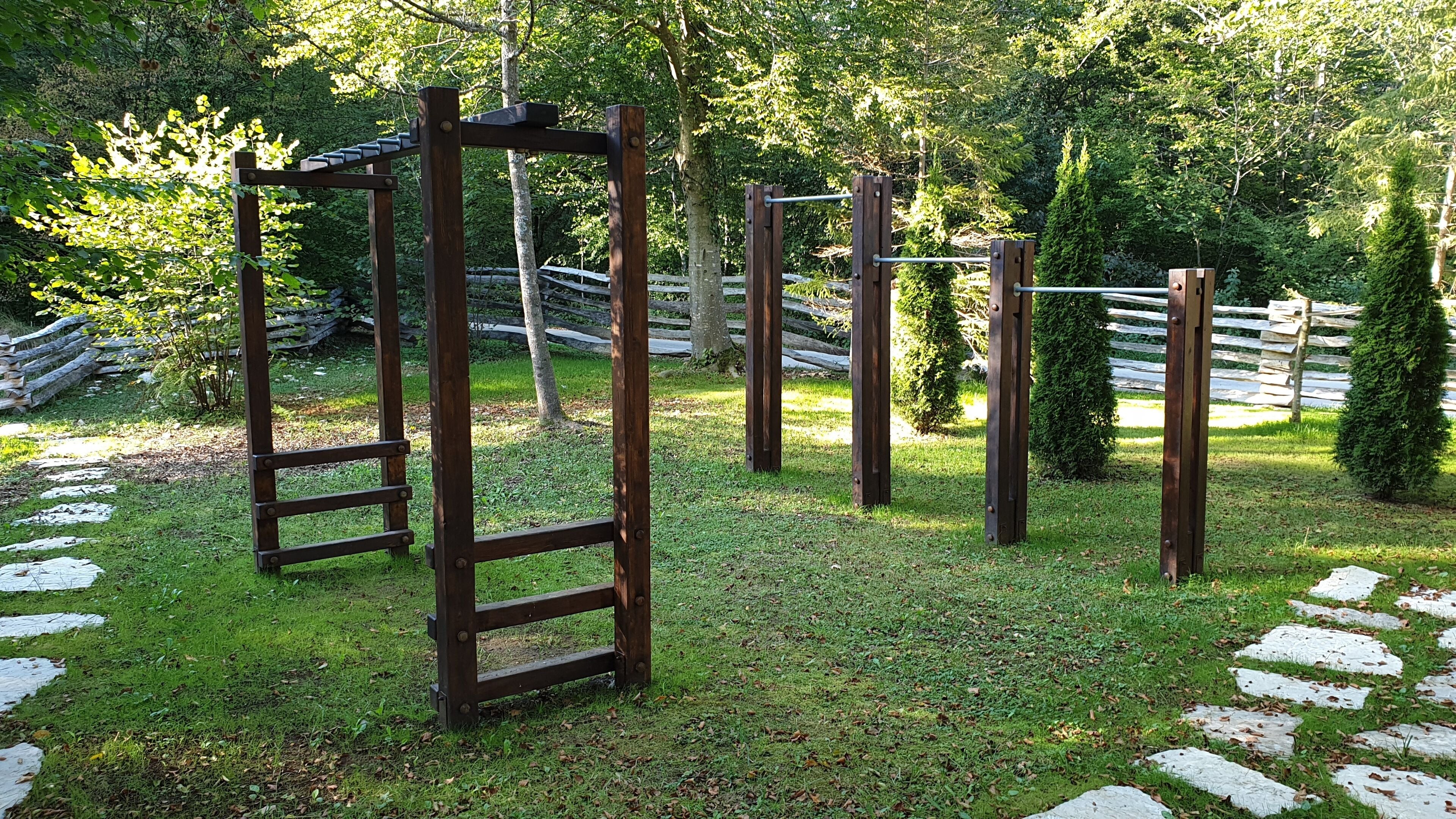 A wooden outdoor gym with various exercise equipment, surrounded by a grassy area and a wooden fence.