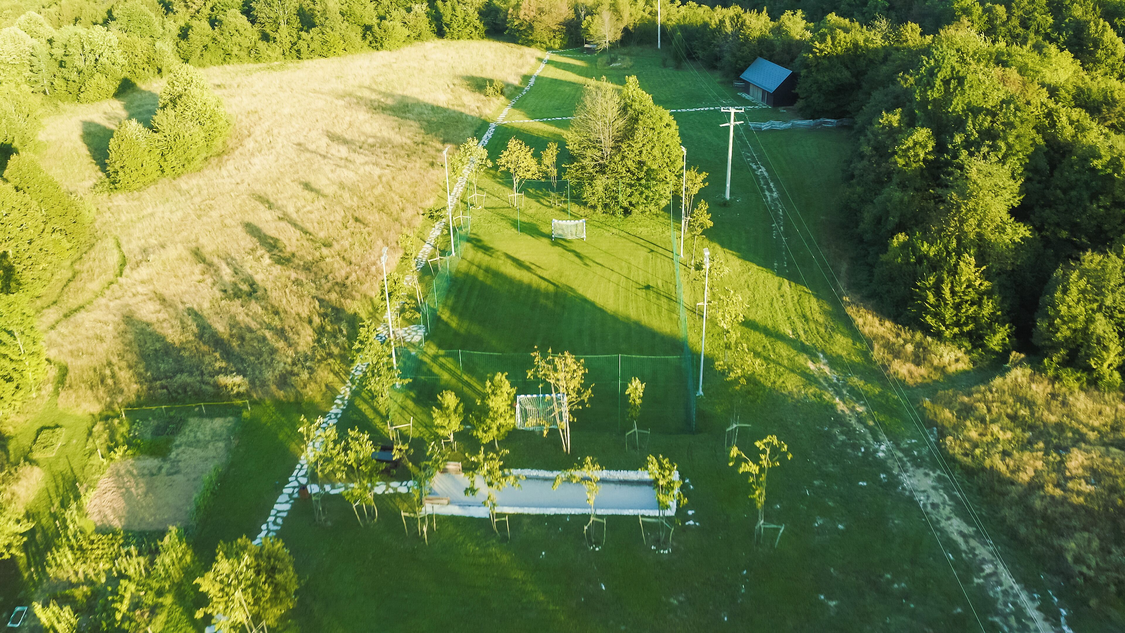 Vista aérea de uma propriedade rural com um campo de futebol cercado, um pequeno edifício e árvores ao redor.