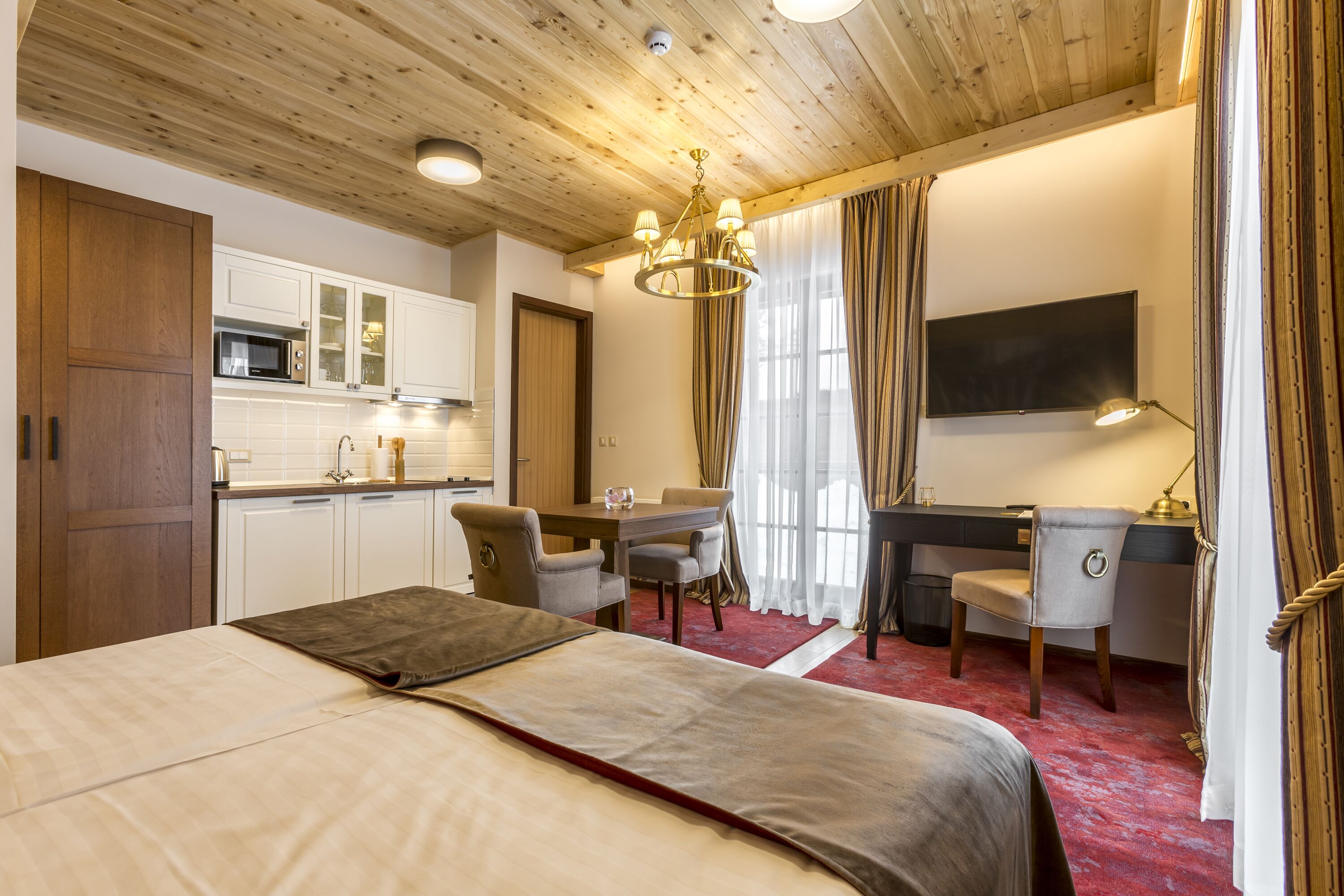 A hotel room with a bed, desk, chair, and kitchenette.