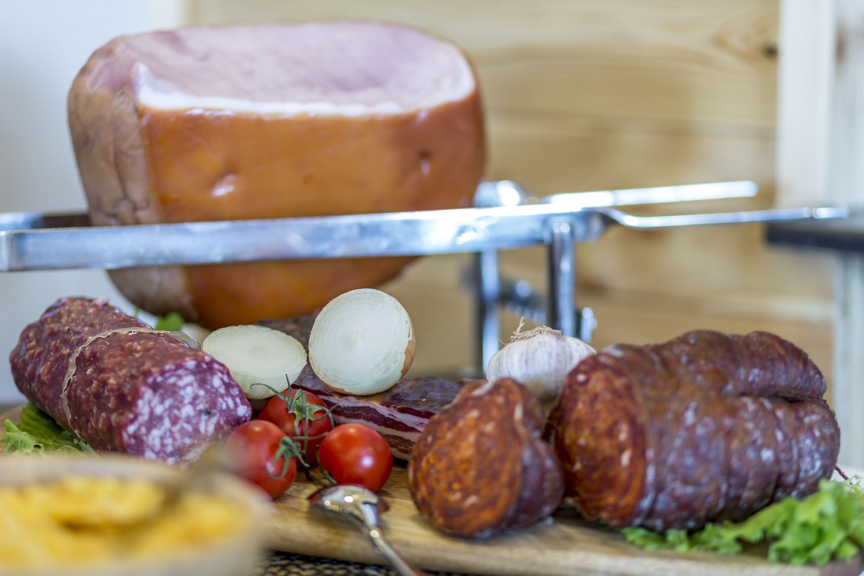 A variety of cured meats and cheeses on a wooden board, with a large ham in the background.