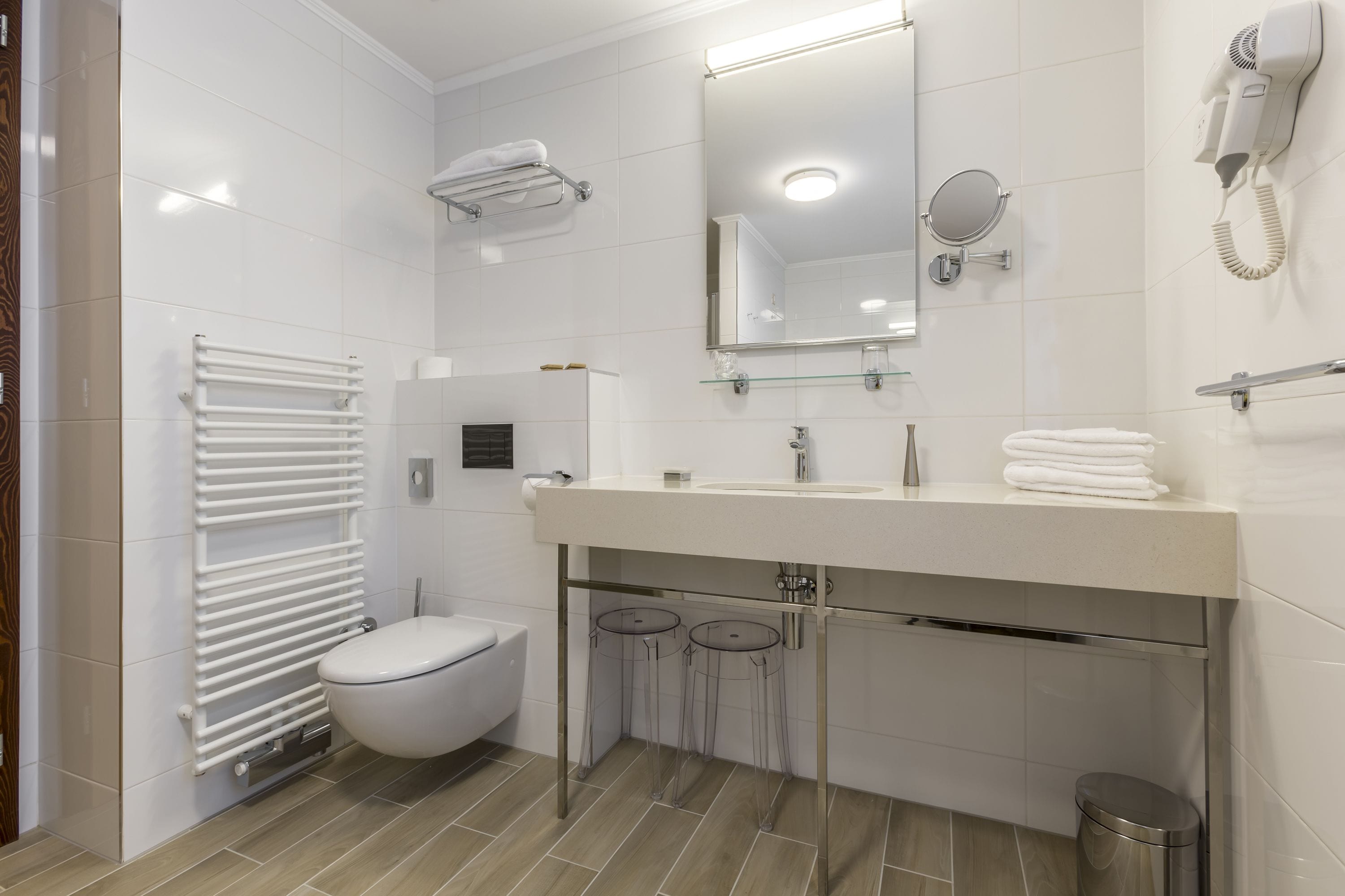 Een moderne badkamer met een wit toilet, een wastafel met spiegel erboven, een handdoekrek en een haardroger aan de muur.