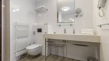 Een moderne badkamer met een wit toilet, een wastafel met spiegel erboven, een handdoekrek en een haardroger aan de muur.