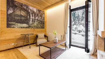 Una habitación acogedora con paredes de madera, un ventanal con cortinas, una mesa de madera, un sofá y un cuadro de una cascada.
