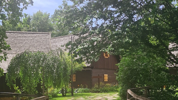 A wooden bridge leading to a rustic building with a thatched roof, surrounded by lush greenery. - Fenomen Plitvice (Plitvicka Jezera)