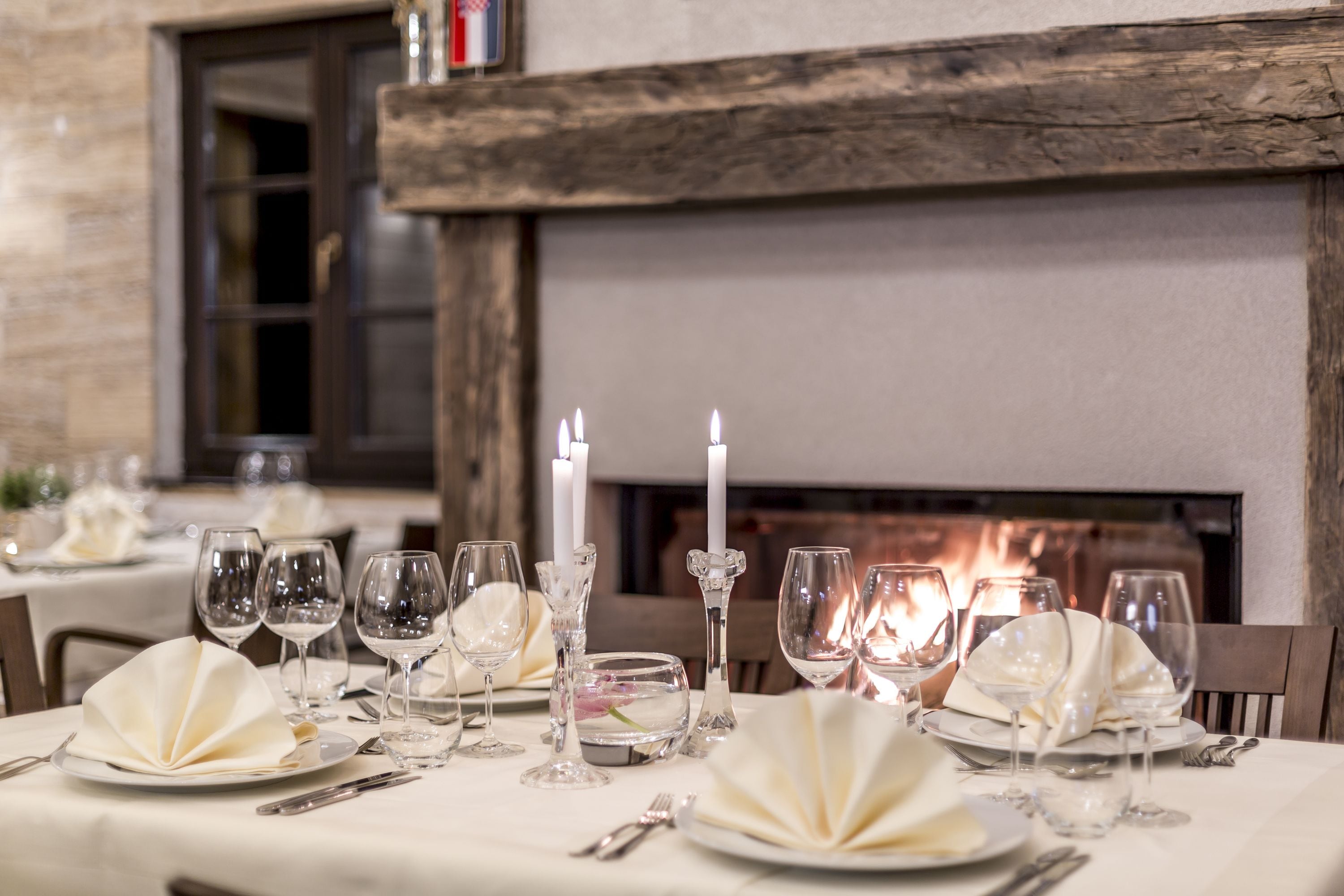 Una mesa de comedor adornada con manteles blancos, copas de cristal y velas.