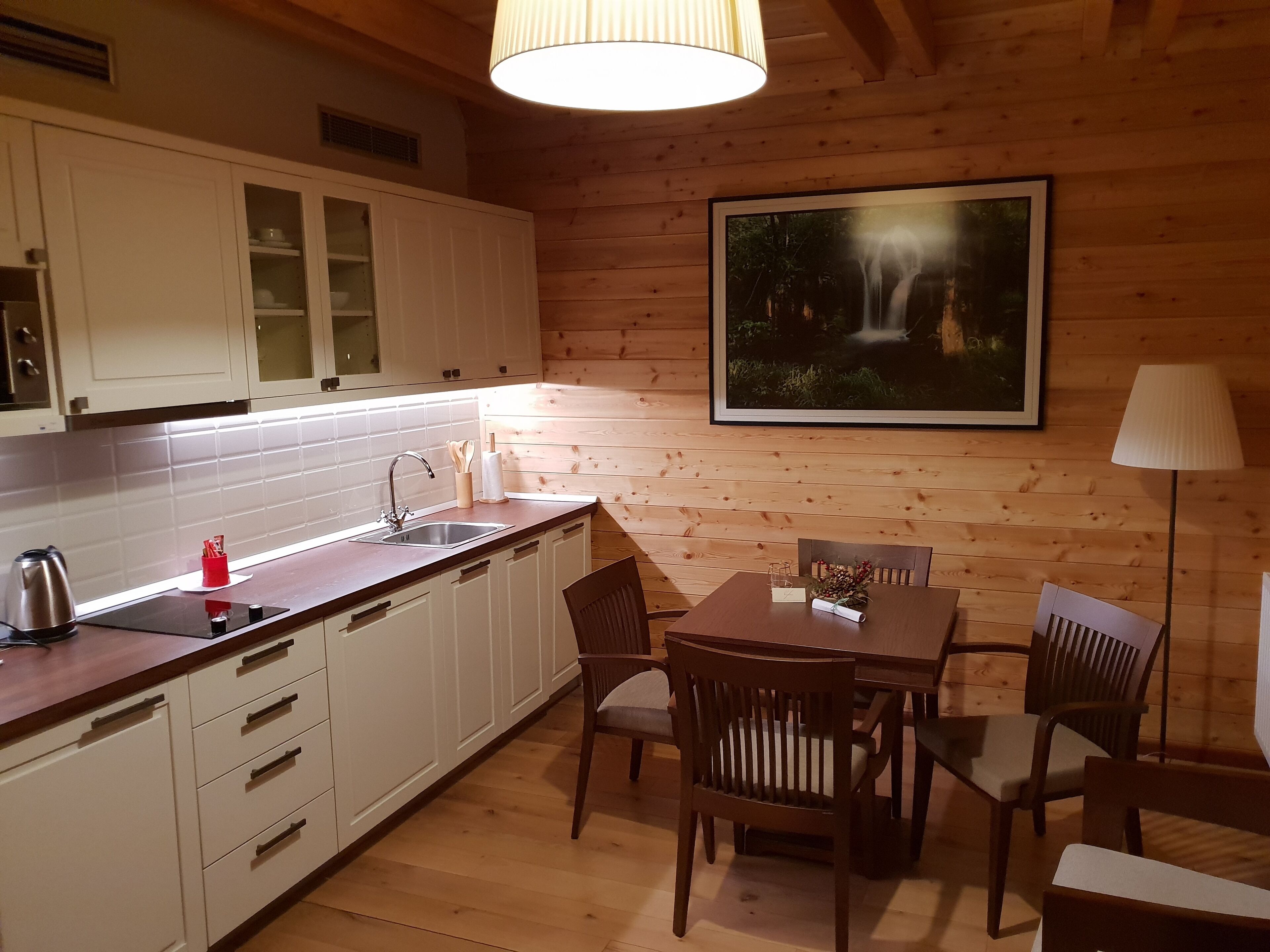 A wooden interior with a kitchen area, dining table, chairs, and a framed picture on the wall.
