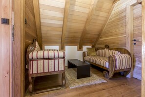 A cozy attic room with wooden walls and a sloped ceiling. It features a striped sofa, a small wooden table, and a rug on the wooden floor.