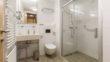 A modern bathroom with a glass shower enclosure, a toilet, and a sink with a mirror above it.