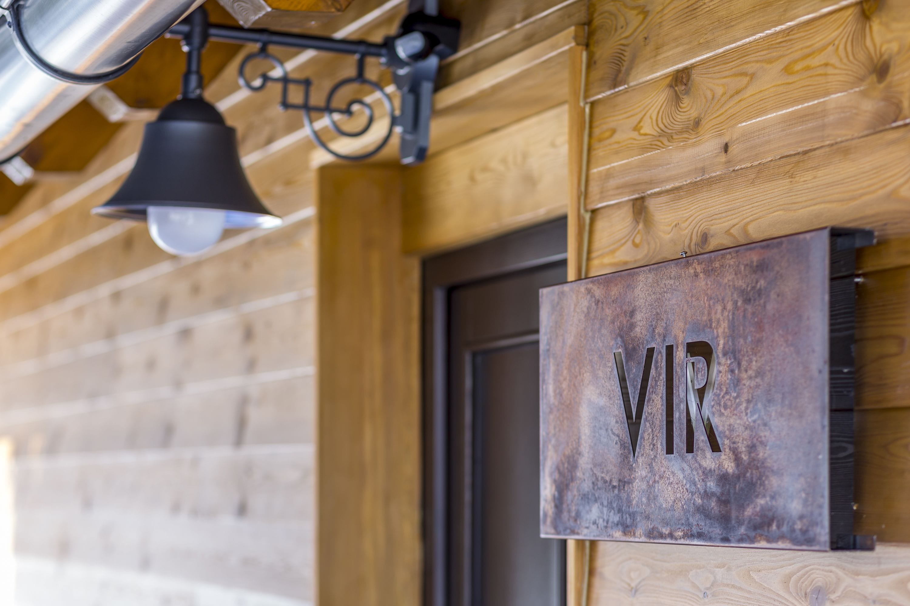 A rustic wooden wall with a metal sign reading "VR" and a black bell hanging from a metal fixture.