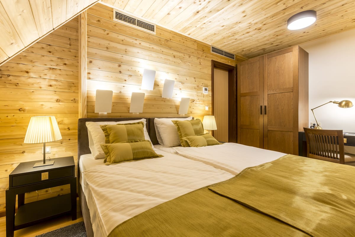Ein Schlafzimmer mit Holzwandverkleidung, zwei Betten, Nachttischlampen und einem Schreibtisch mit Stuhl.