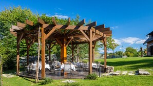 A wooden pergola with tables and chairs set up underneath, surrounded by a grassy area and trees. - Fenomen Plitvice (Plitvicka Jezera)